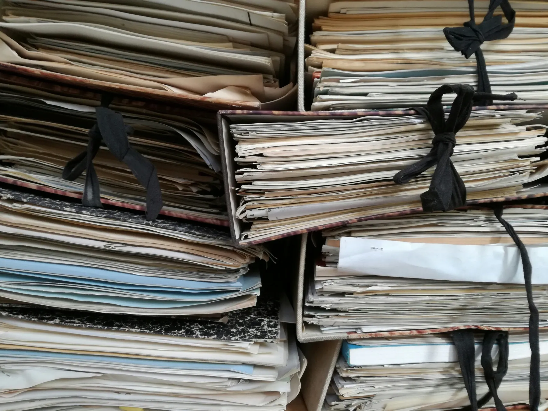 Carpetas de archivo llenas de documentos y atadas con cinta, apiladas en un armario.