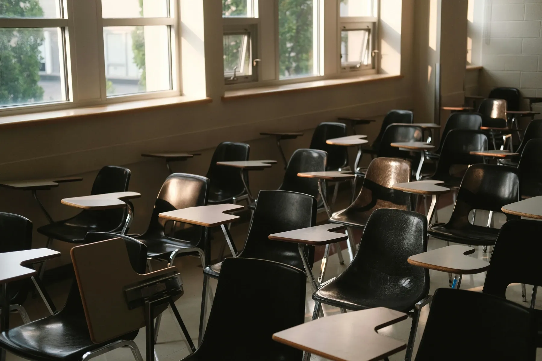 Un aula vacía con filas de sillas de pala junto a los ventanales.