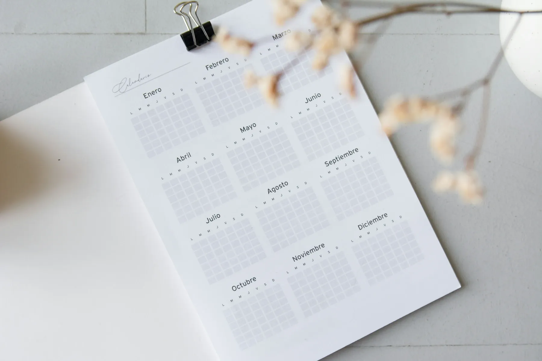 Un calendario anual en papel, con los meses en español, sujeto con una pinza sobre la mesa.