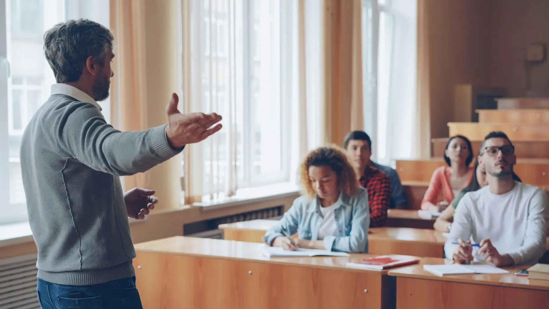 Un profesor explica la lección a un grupo de alumnos adultos que toman notas en el aula.