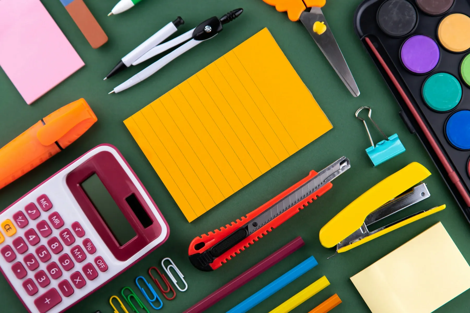 Material de papelería ordenado sobre una mesa: notas adhesivas, subrayadores, calculadora y clips.