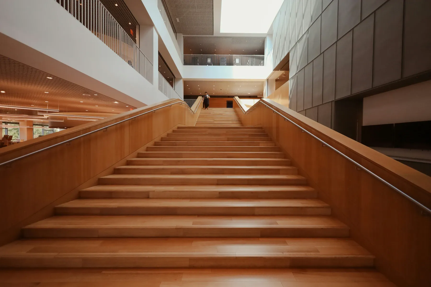 Una escalera ancha de madera que sube entre las plantas de un edificio de oficinas.
